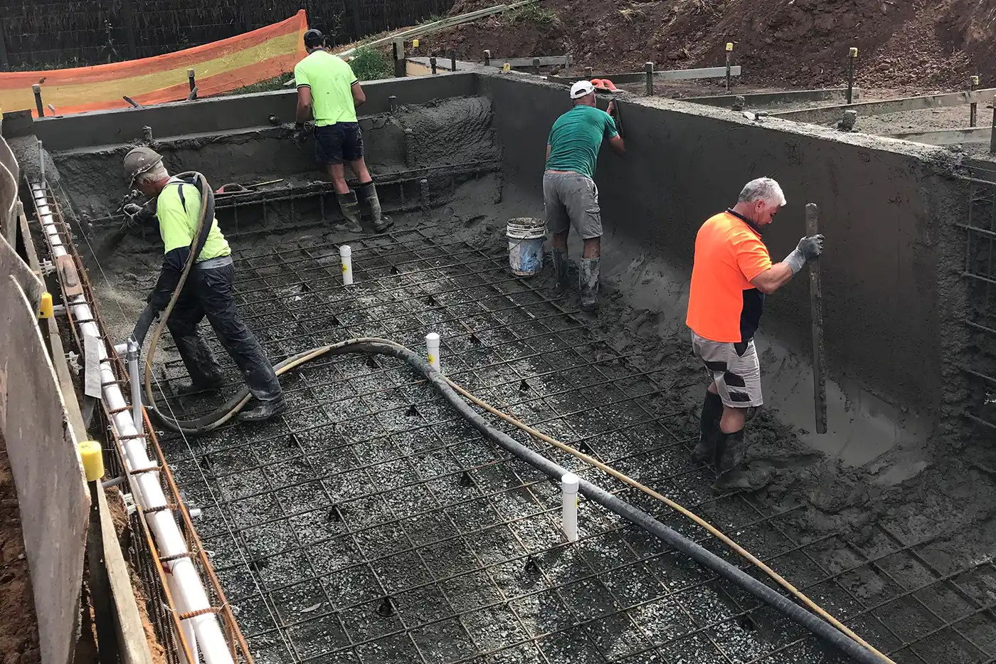 Concrete is sprayed onto the swimming pool frame while workers trowel it smooth Swimming Pool Construction Shepparton